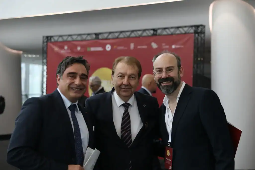 Three men in formal attire smiling at a professional gathering.
