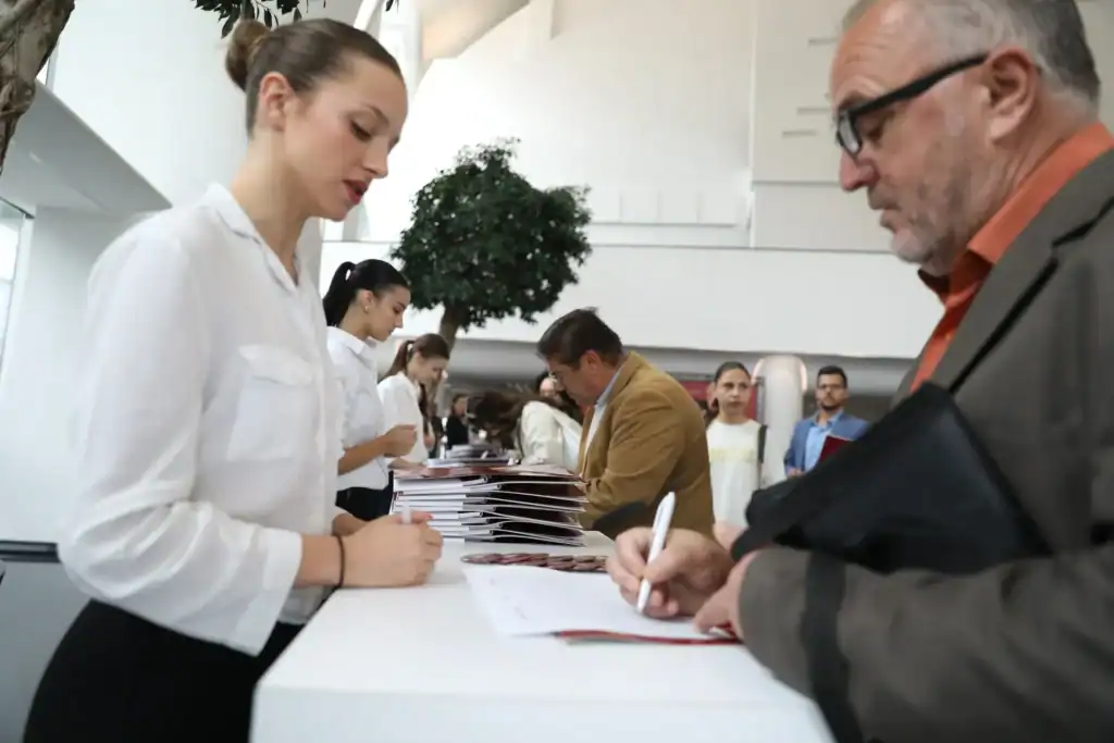 A young woman and an older man completing registration forms at a busy event desk.
