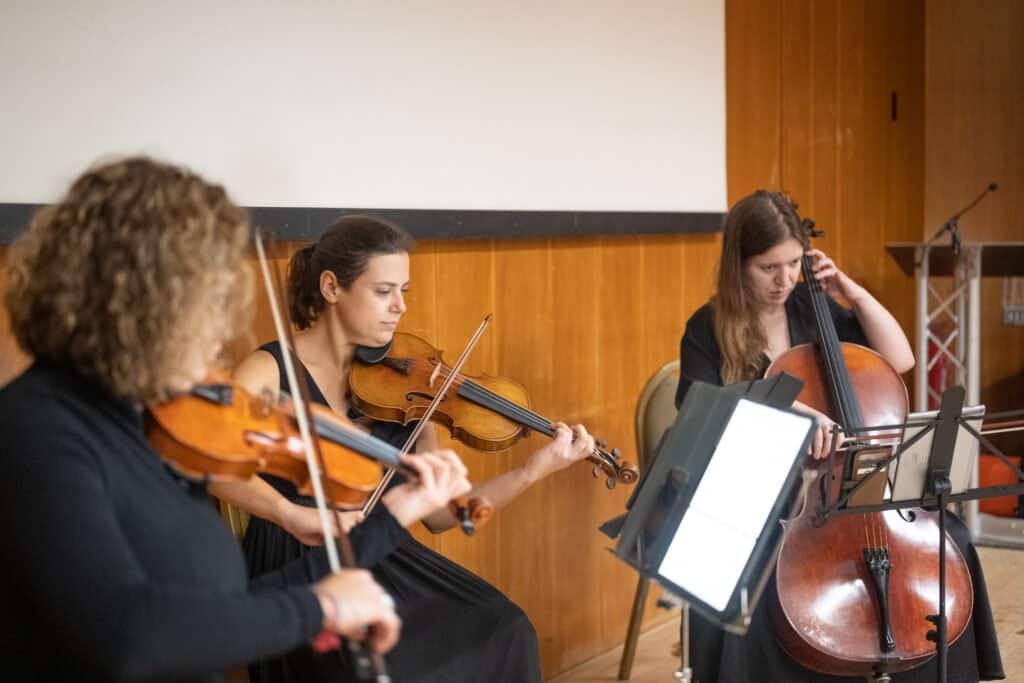 Three women playing string instruments during a rehearsal or concert.