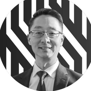 Man in glasses smiling, black and white background, professional headshot.