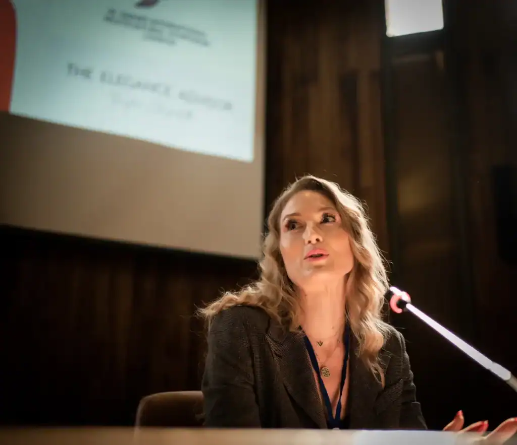 Woman speaking at a conference with a presentation slide in the background.